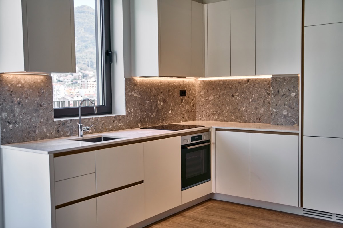 Moderne Küche in einer Wohnung in Tivat, Montenegro: weiße Fronten, Terrazzo-Spritzschutz und Bergblick aus dem Fenster.