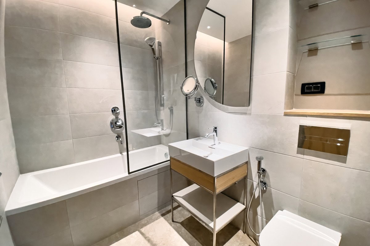 Modernes Badezimmer in einer Wohnung in Tivat, Montenegro: helle Fliesen, Badewanne mit Glasabtrennung, stilvolle Sanitäranlagen.
