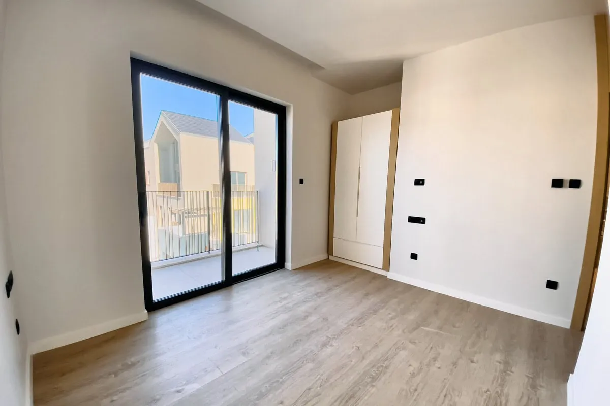Helles Schlafzimmer in einer Wohnung in Tivat, Montenegro: Panoramafenster, Zugang zum Balkon, Einbauschrank und Laminatboden.