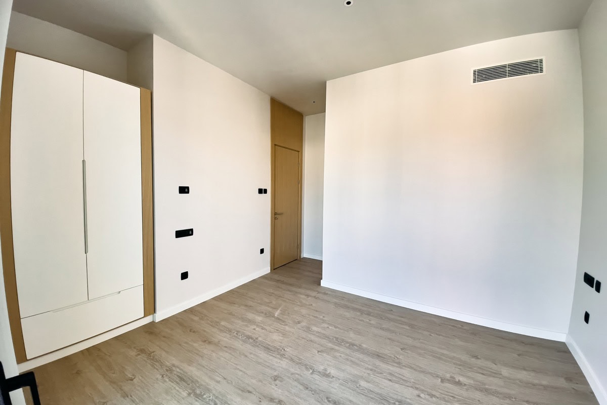 Helles Schlafzimmer mit weißem Kleiderschrank und Laminat in einer neuen Wohnung in Tivat, Montenegro. Moderne Ausstattung und Klimaanlage.