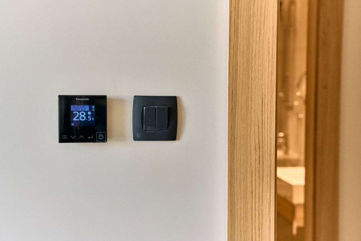 Panasonic-Thermostat und Lichtschalter in einer modernen Wohnung in Tivat, Montenegro, mit Holzoptik.