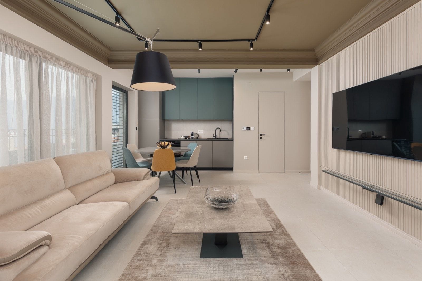 Nowoczesny salon z kuchnią w mieszkaniu w Dobrocie, Czarnogóra: beżowa sofa, stylowe meble i oświetlenie szynowe.