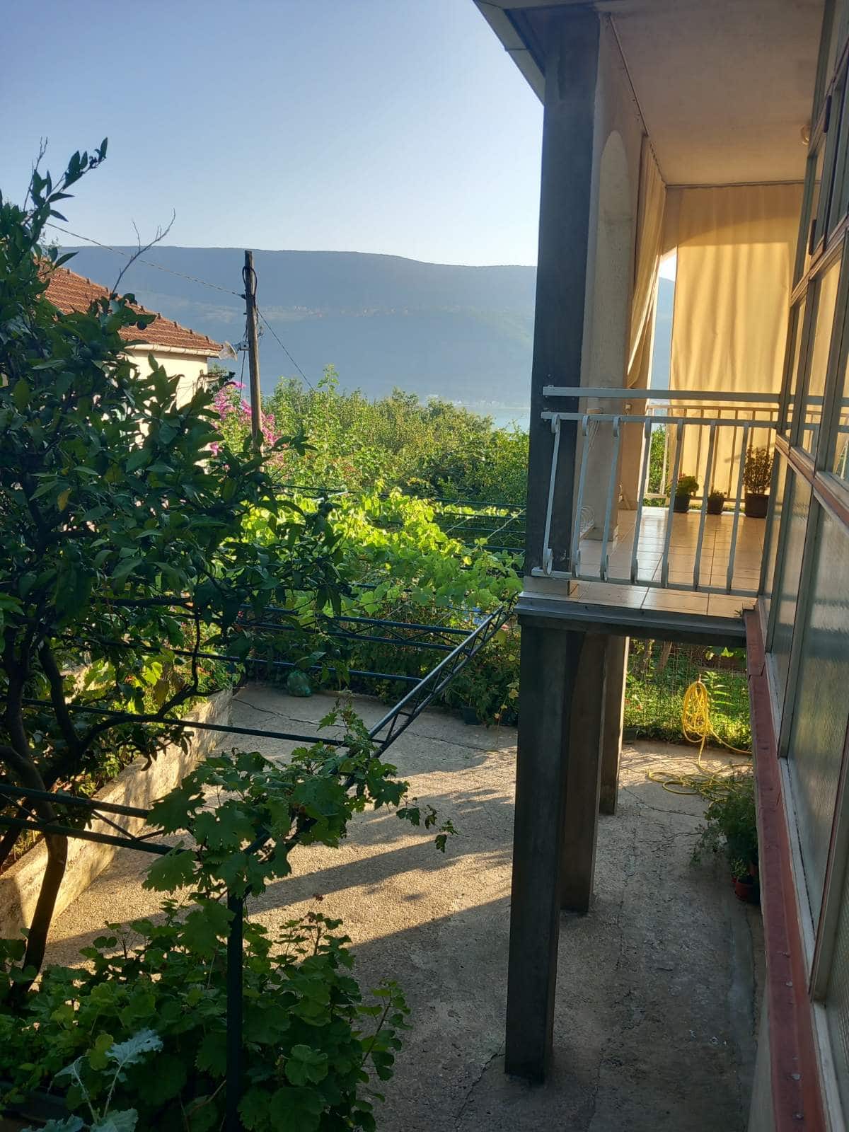 Balcony of a house in Igalo, Montenegro, overlooking a green garden and mountains, terrace with an awning and outdoor furniture.