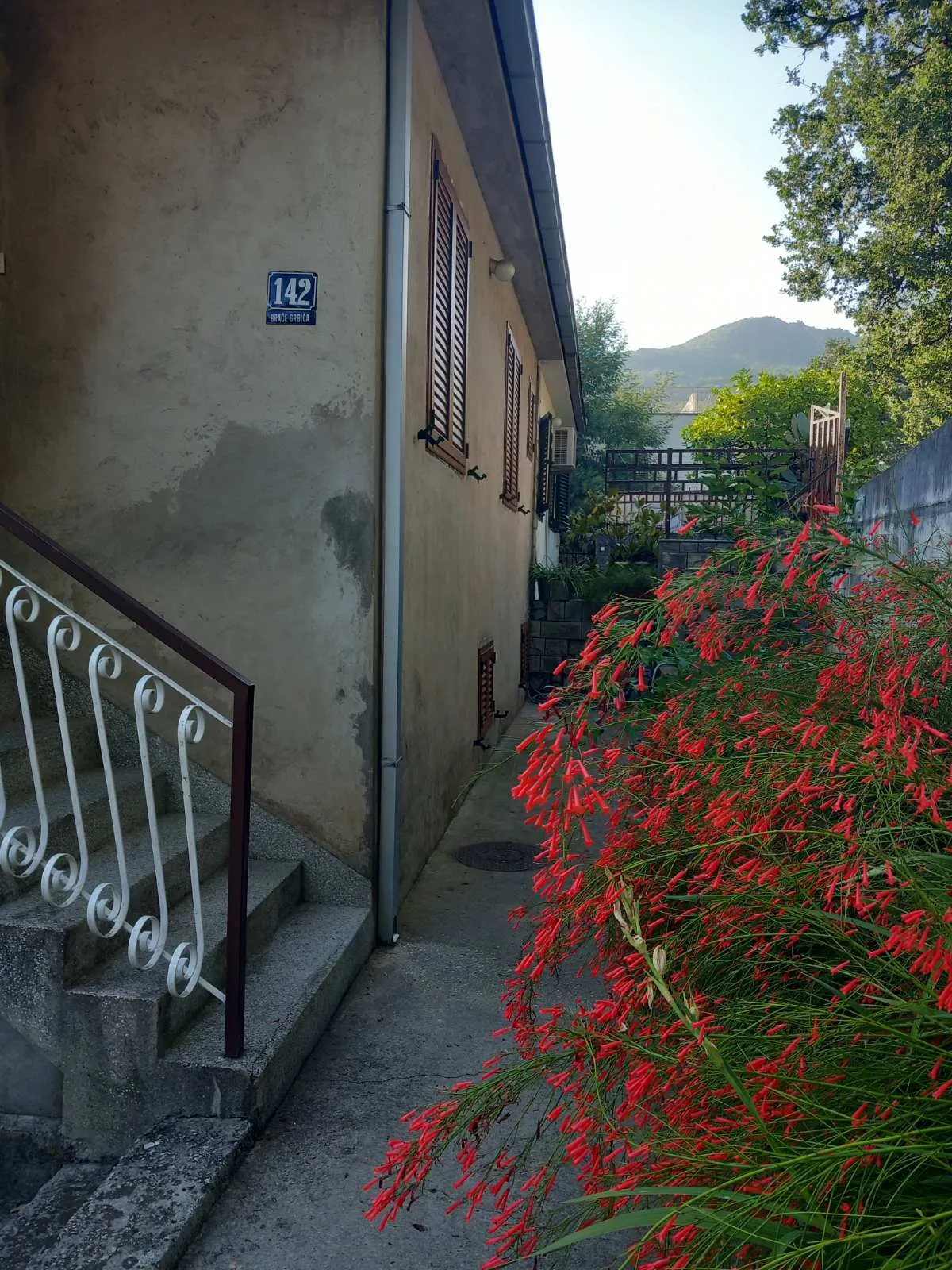 Fassade eines Hauses in Igalo, Montenegro: Steintreppe, blühender Garten und Bergblick in einer ruhigen Wohngegend.