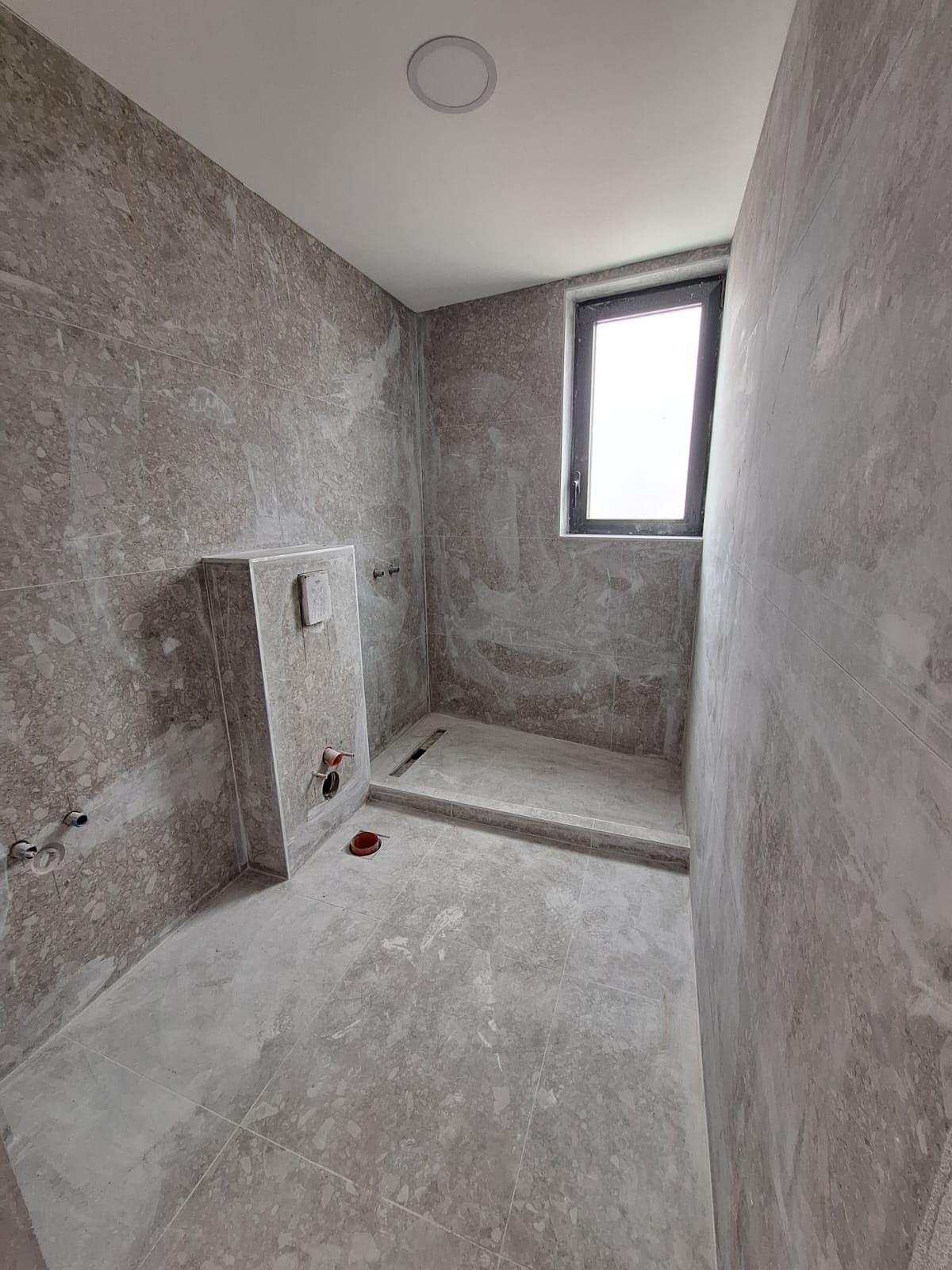 Bar, Karadağ’daki dairede tadilat sürecindeki banyo: gri fayans, duş alanı ve gömme rezervuar.