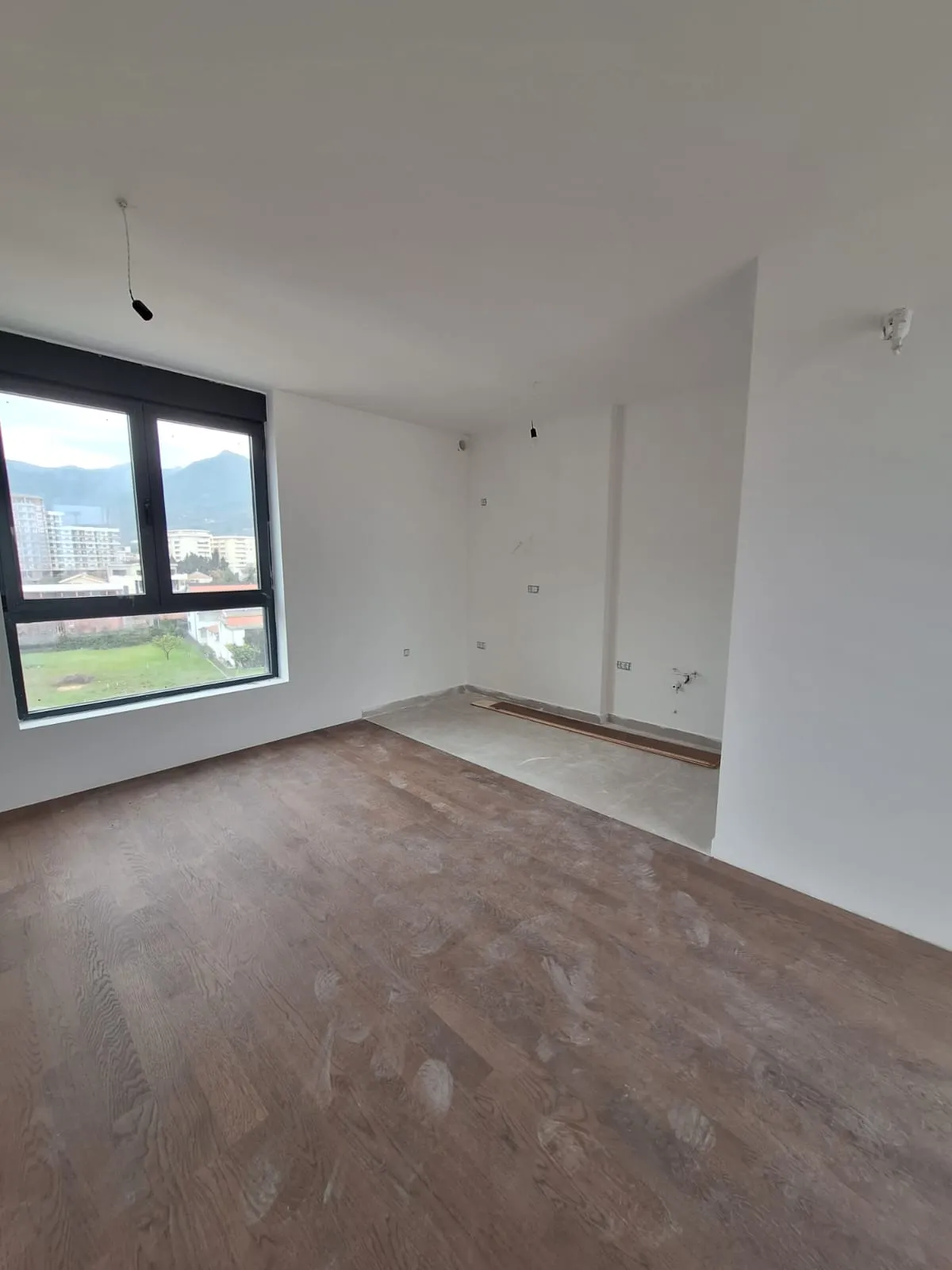 Unfinished room with wooden floor, window, and white walls.