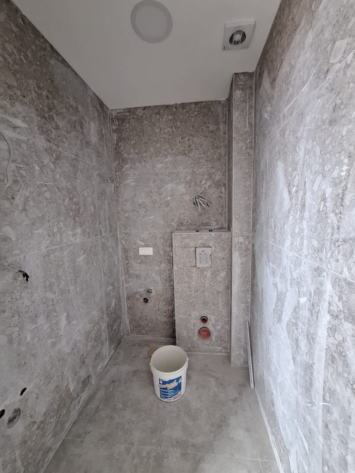 Bar, Karadağ'daki dairede banyo tadilatı: duvarlar gri taş görünümlü fayansla kaplı, gömme klozet montajı.