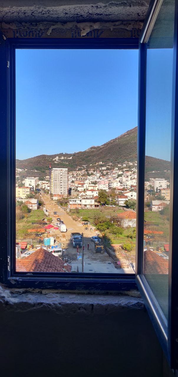 Karadağ, Bar şehrindeki dairenin penceresinden görünüm: güneşli bir দিনে şehrin panoraması, dağlar ve inşaat alanı.