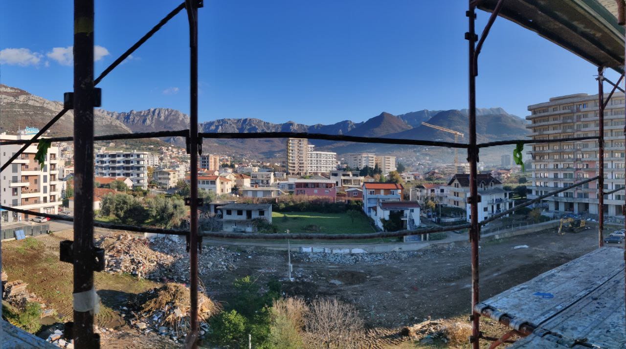 İnşaat halindeki binanın balkonundan Bar şehri ve Karadağ’daki dağların manzarası, ön planda iskeleler.
