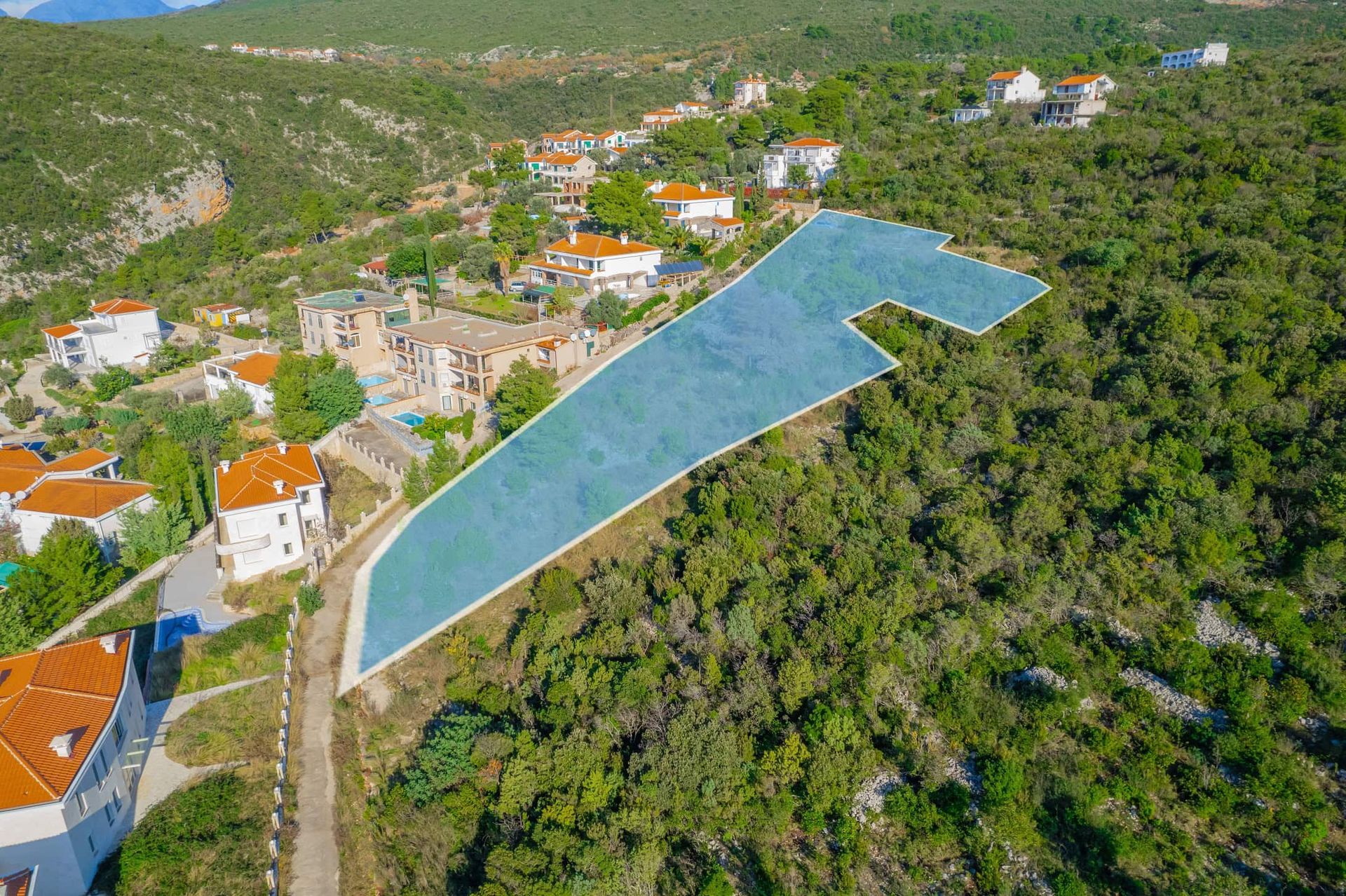 Građevinsko zemljište br. 2390 u Žanjicama, Crna Gora: pogled iz vazduha na parcelu okruženu brdima i vilama.