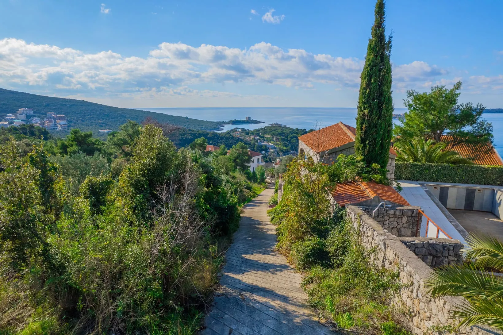 Land plot in Žanjice, Montenegro: panoramic view of the sea, hills, and Mediterranean nature with a path leading to the house.