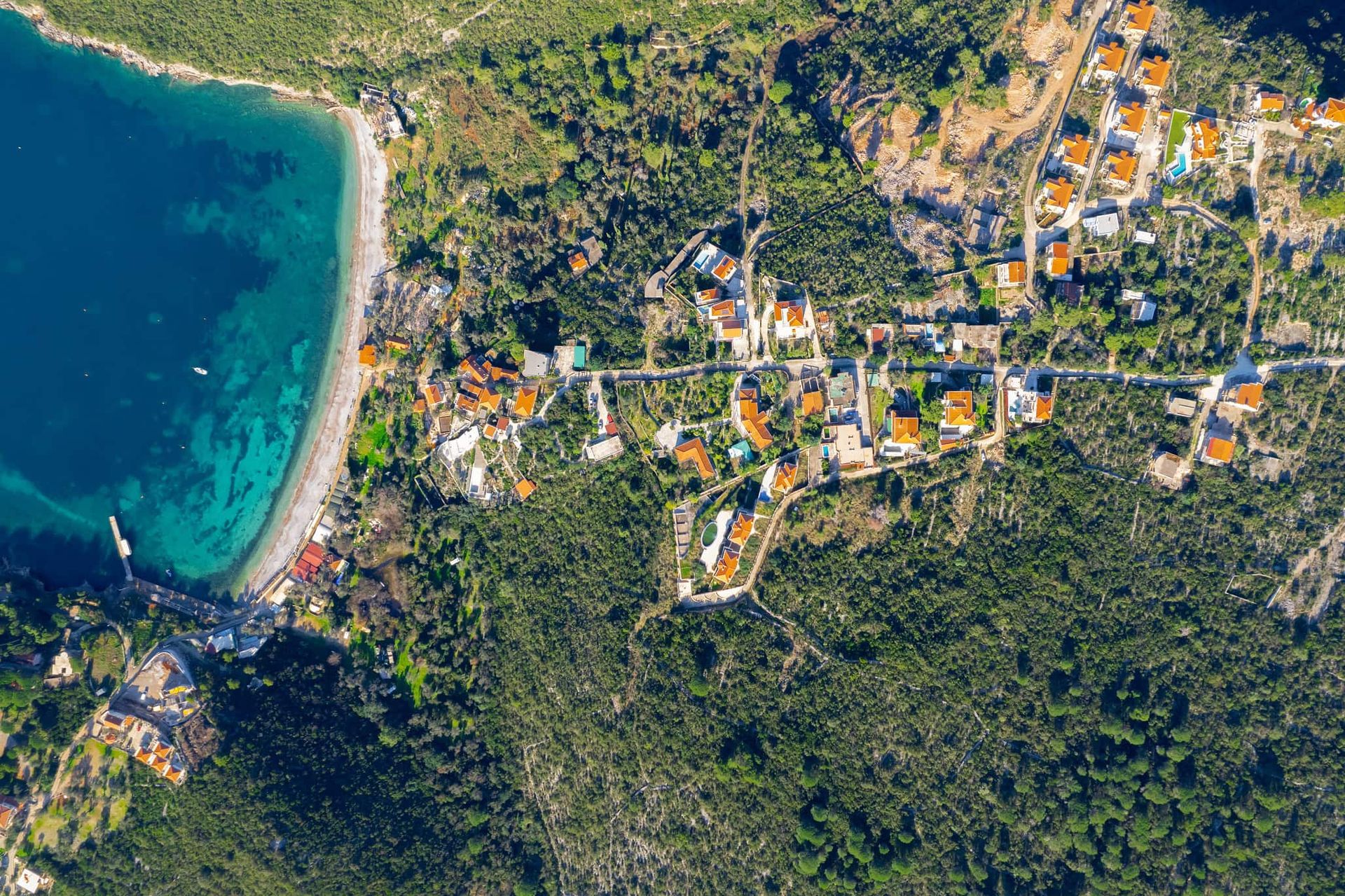 Pogled iz vazduha na zemljište u Žanjicama, Crna Gora: obalni pojas, zelena brda i stambeni objekti pored mora.