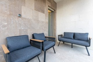 Gemütliche Villa-Terrasse in Bečići, Montenegro: moderne Gartenmöbel mit grauen Polstern und Wandverkleidung aus Naturstein.