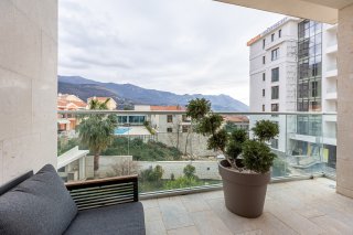 Balkon einer Villa in Bečići, Montenegro: Bergblick, moderne Möbel, Glasgeländer und eine Zierpflanze.