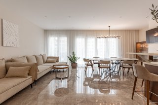 Modernes Wohnzimmer mit beigem Sofa und Essbereich in einer Villa in Bečići, Montenegro, Marmorboden und Panoramafenster.