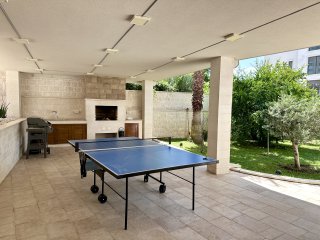Überdachte Terrasse mit Grillplatz und Tischtennisplatte in einer Villa in Bečići, Montenegro, mit Zugang zum grünen Garten.