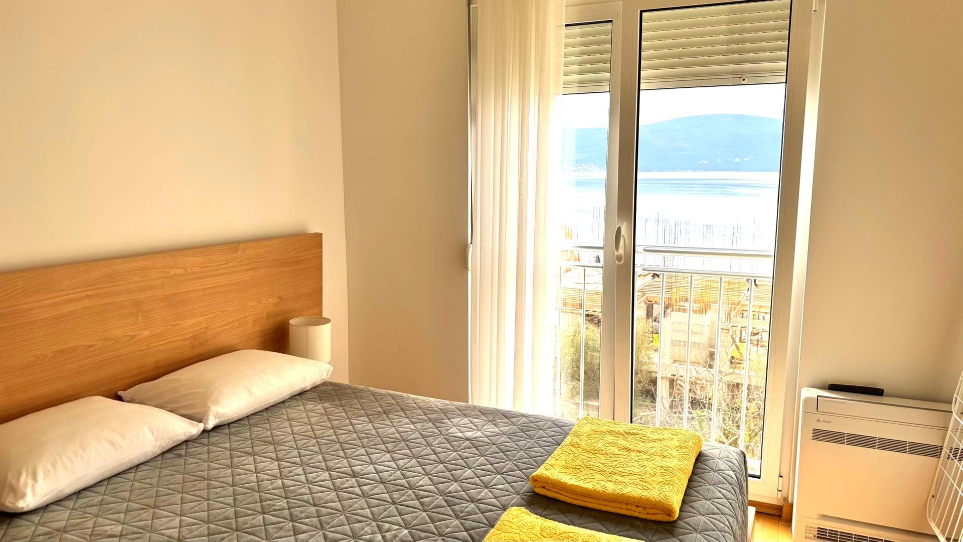Spavaća soba u stanu u Tivtu, Crna Gora: bračni krevet, svetla završna obrada i balkon s panoramskim pogledom na more.