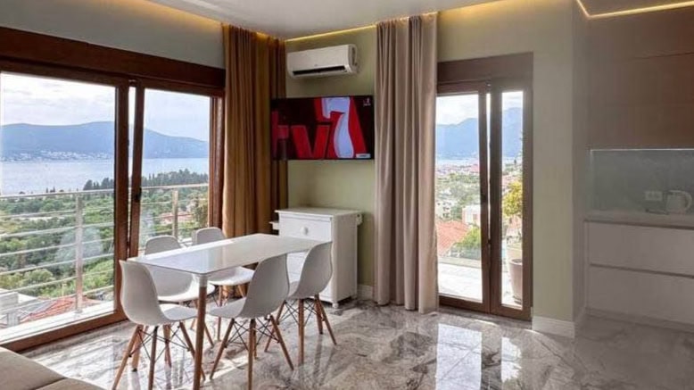 Dnevna soba s panoramskim pogledom na more u stanu u Tivtu, Crna Gora: moderan nameštaj, mermerni pod i terasa.