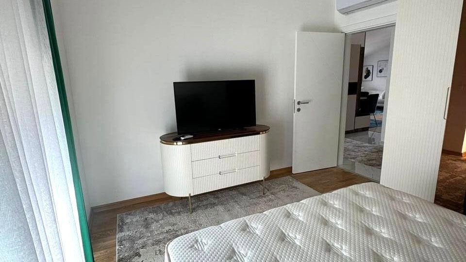 Modernes Schlafzimmer mit weißer Kommode und TV in einer Wohnung in Tivat, Montenegro: stilvolles Interieur mit Parkettboden.