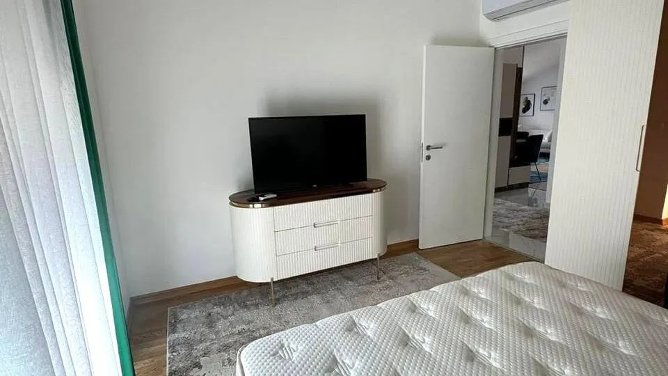 Modernes Schlafzimmer mit weißer Kommode und TV in einer Wohnung in Tivat, Montenegro: stilvolles Interieur mit Parkettboden.