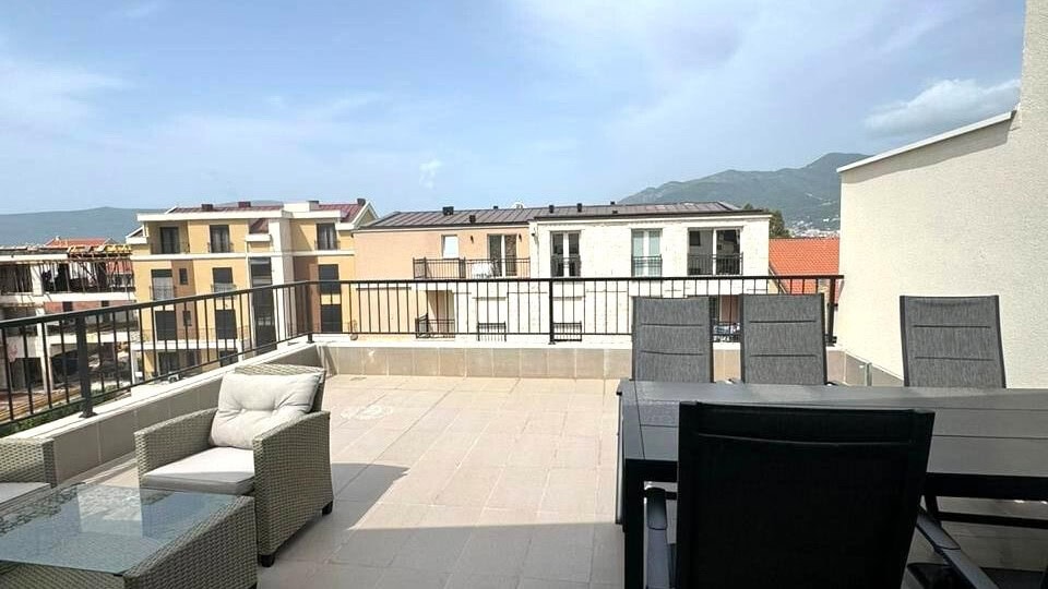 Geräumige Terrasse mit Gartenmöbeln in einer Wohnung in Tivat, Montenegro, mit Blick auf die Berge und die Stadtbebauung.