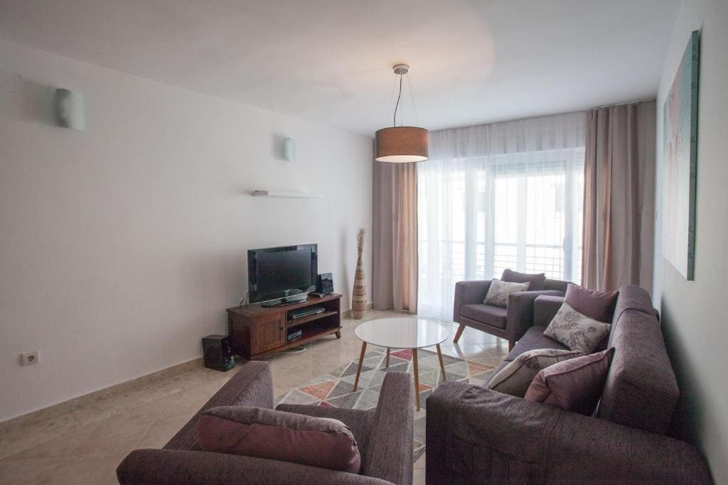 Gemütliches Wohnzimmer mit Polstermöbeln und Zugang zum Balkon in einer Wohnung in Budva, Montenegro. Modernes Interieur.