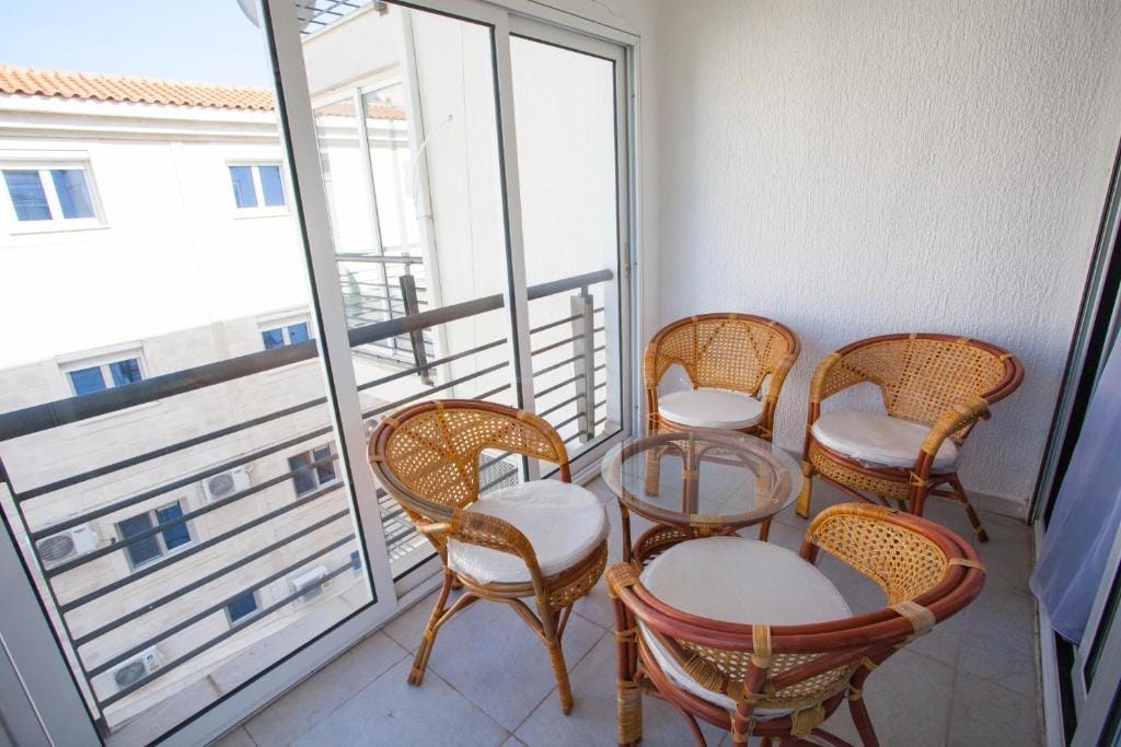 Gemütlicher Balkon mit Rattanmöbeln in einer Wohnung in Budva, Montenegro: Glastisch und vier Sessel mit Kissen.