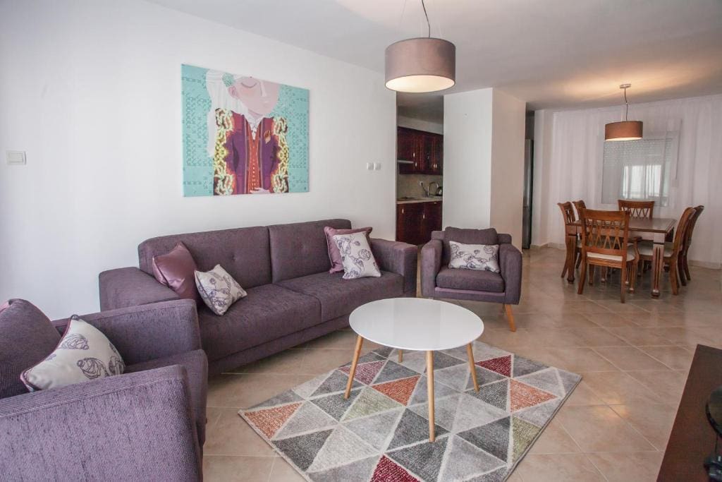 Wohnzimmer mit violetter Polstermöbelgarnitur und Essbereich in einer Wohnung in Budva, Montenegro. Modernes Interieur.