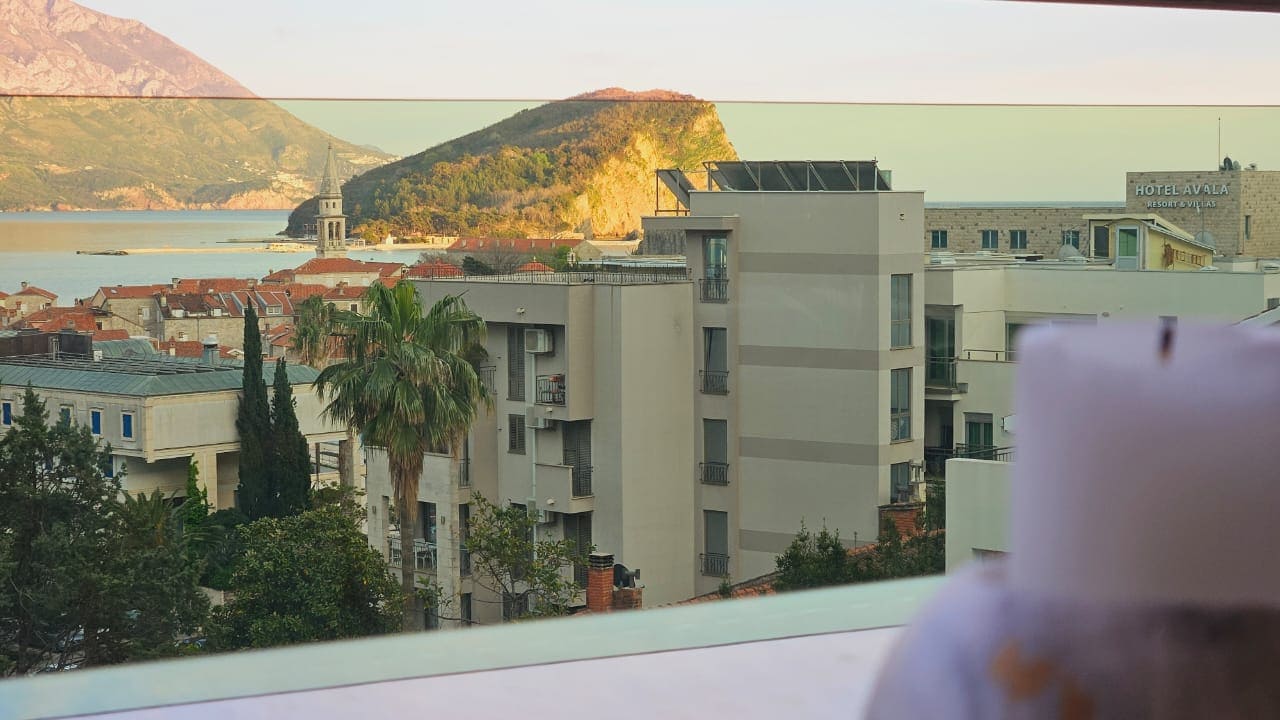 Blick vom Balkon einer Wohnung in Budva, Montenegro: Panorama der Altstadt, des Hotels Avala, der Berge und der Adria.