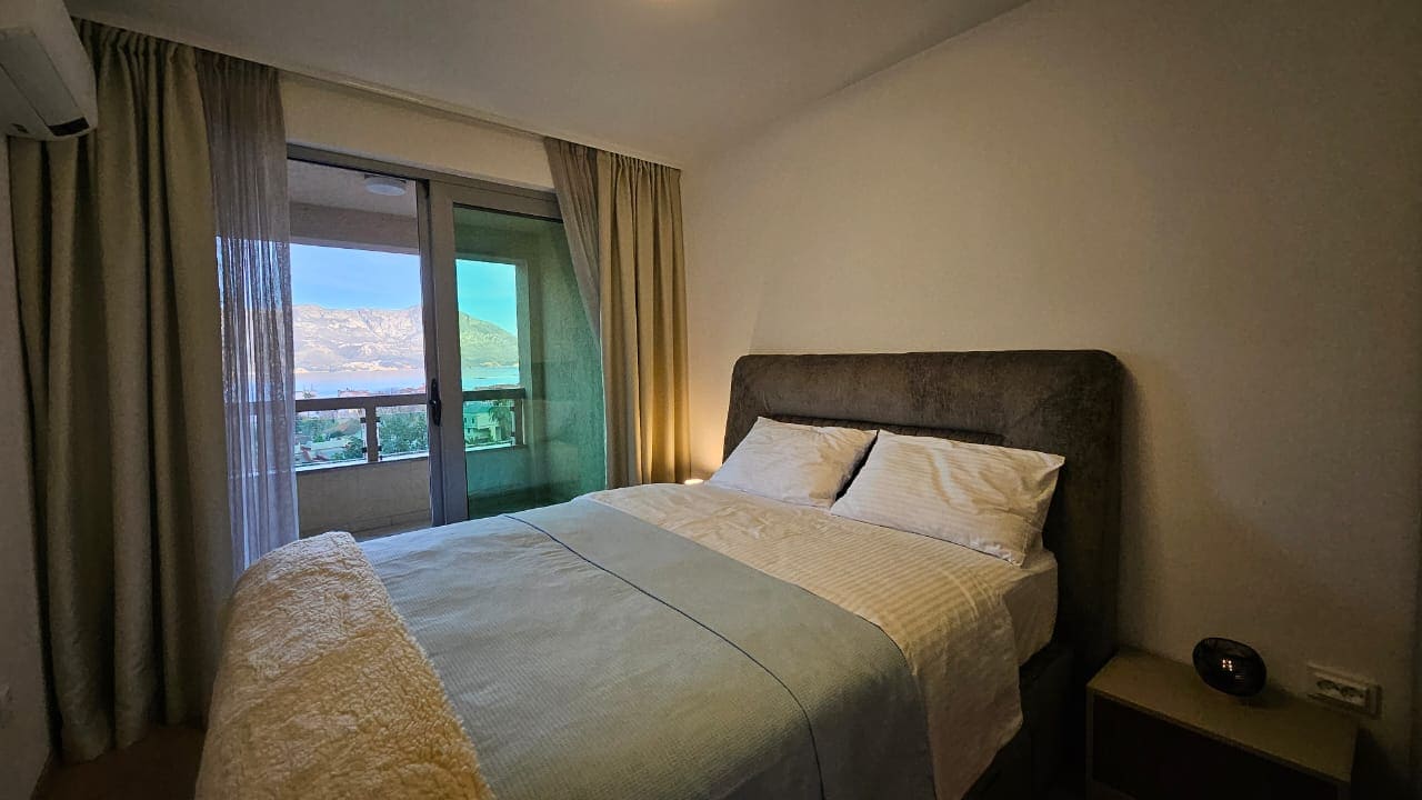 Schlafzimmer in einer Wohnung in Budva, Montenegro: Doppelbett, Panoramafenster mit Blick auf die Berge und das Meer, Balkon.