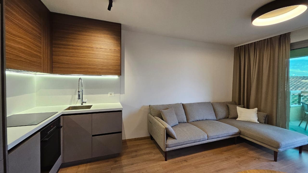 Modernes Wohnzimmer mit Küche in einer Wohnung in Budva, Montenegro: graues Ecksofa, Einbaumöbel und Blick auf die Terrasse.