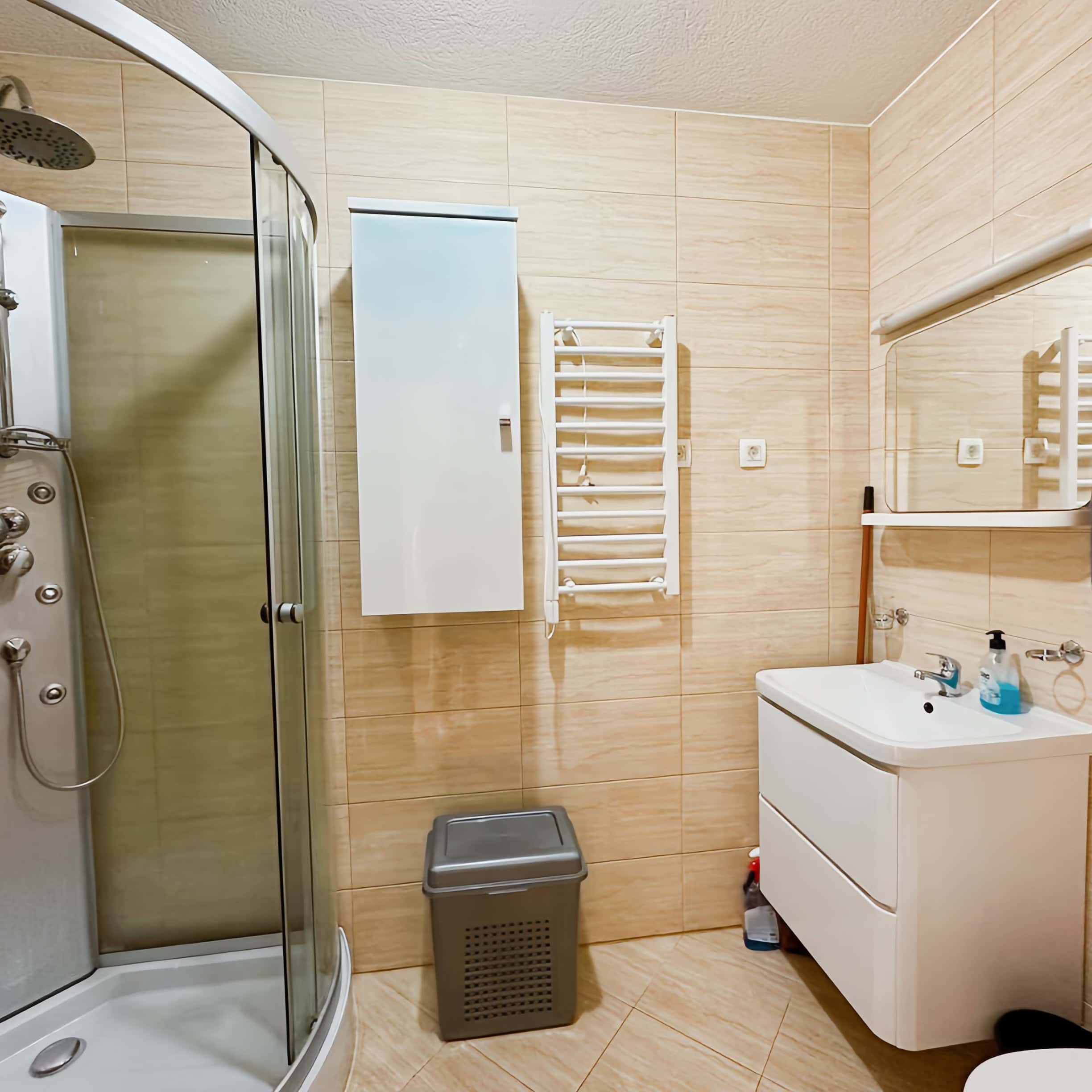 Badezimmer in einer Wohnung in Bečići, Montenegro: Duschkabine, weißer Waschtischunterschrank und Handtuchheizkörper.