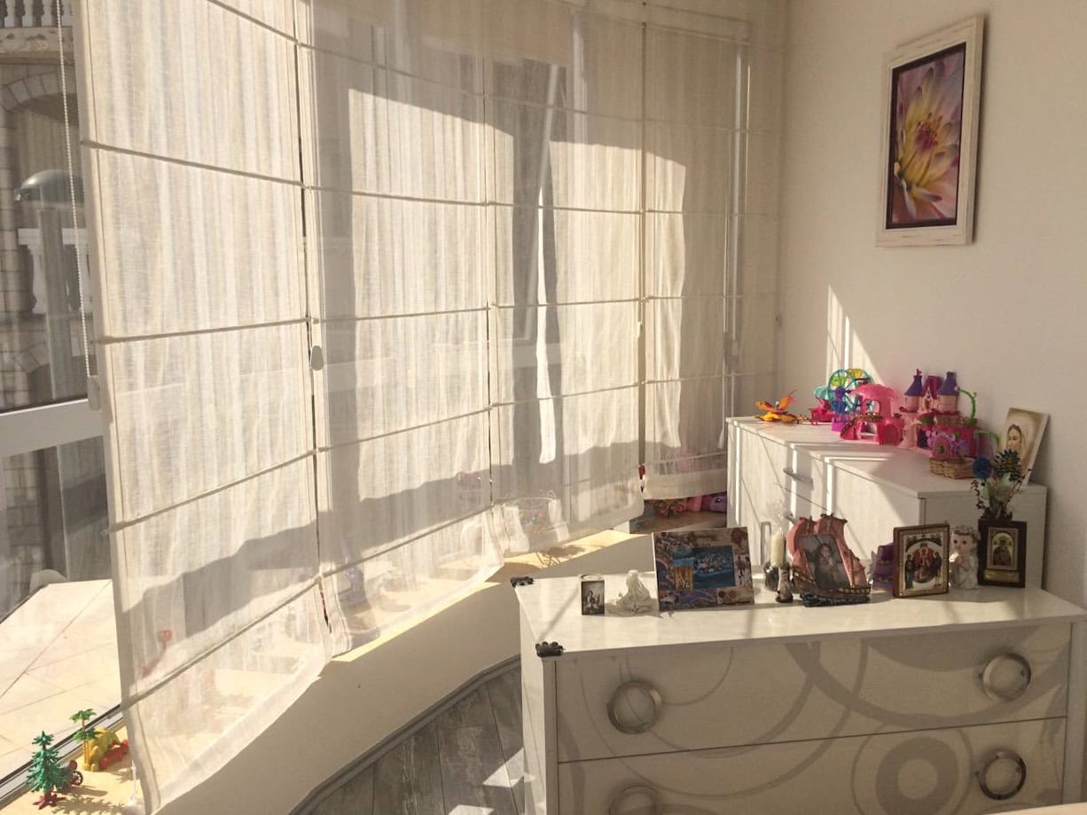 Helles Schlafzimmer in einer Wohnung in Bečići, Montenegro: weiße Möbel, römische Rollos an den Fenstern und Dekor im Interieur.