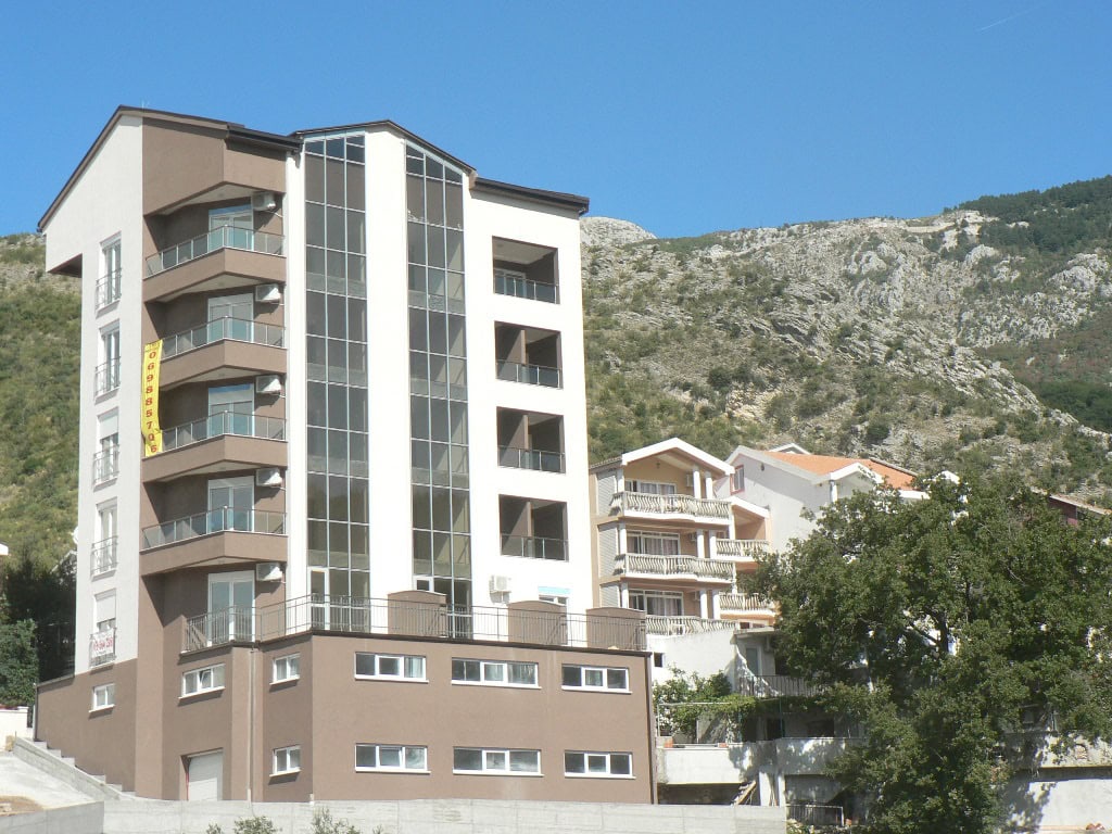 Modernes Wohnhaus mit Panoramafenstern und Balkonen in Bečići, Montenegro, vor Bergkulisse.