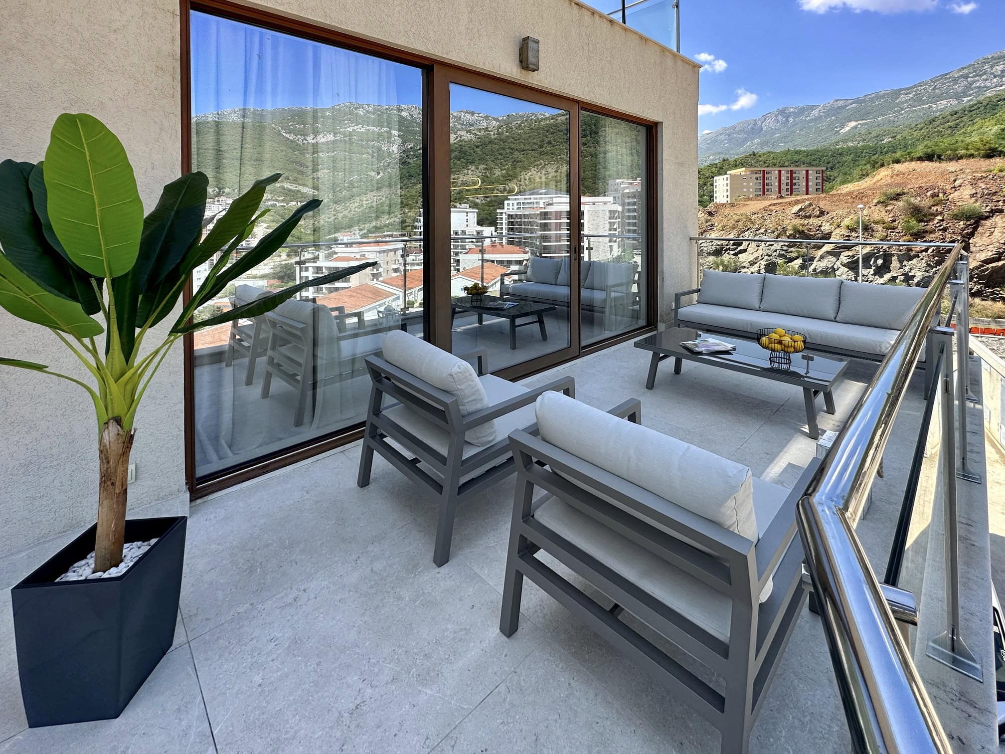Prostrana terasa sa nameštajem i pogledom na planine u stanu u Bečićima, Crna Gora. Moderan balkon sa panoramskim prozorima.