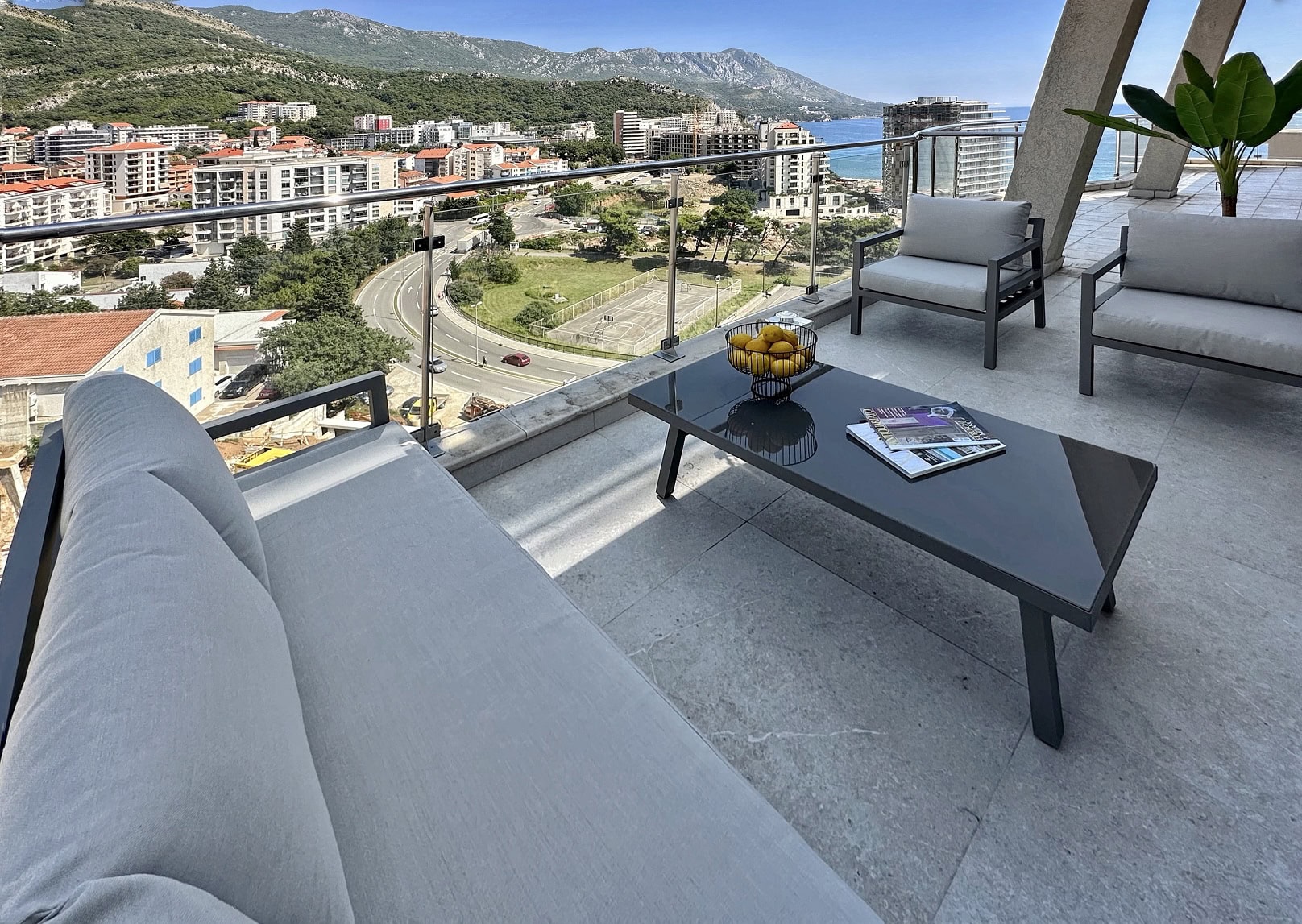 Terasa apartmana u Bečićima, Crna Gora: moderan nameštaj, pogled na more, planine i grad sa panoramskog balkona.