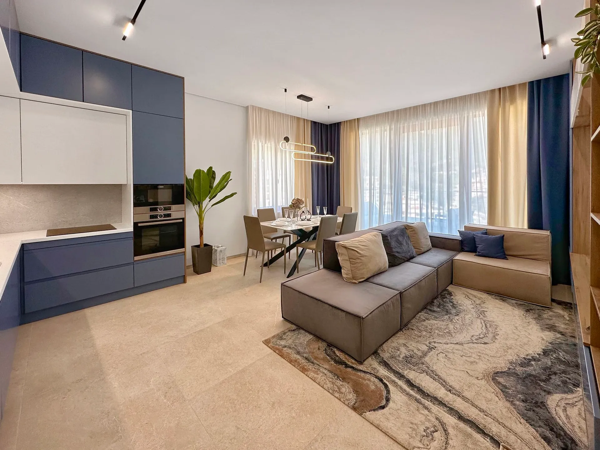 Nowoczesny salon z kuchnią, szarym sofa, stołem do jedzenia i niebieskimi szafkami.