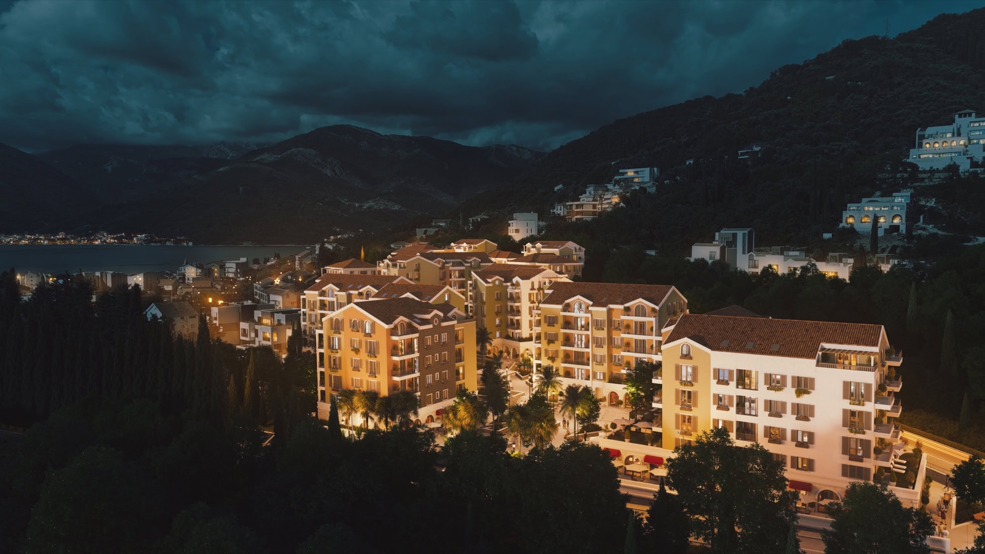 Tivat, Karadağ'daki konut kompleksinin akşam görünümü: aydınlatmalı, teraslı, dağ ve deniz manzaralı modern evler.