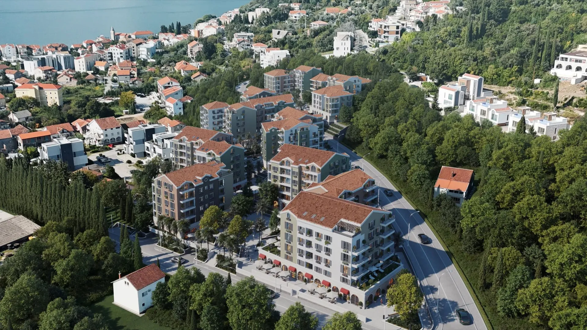 Modern apartman kompleksleri ve yeşil tepelerle çevrili kıyı tatil kasabasının havadan görünümü.