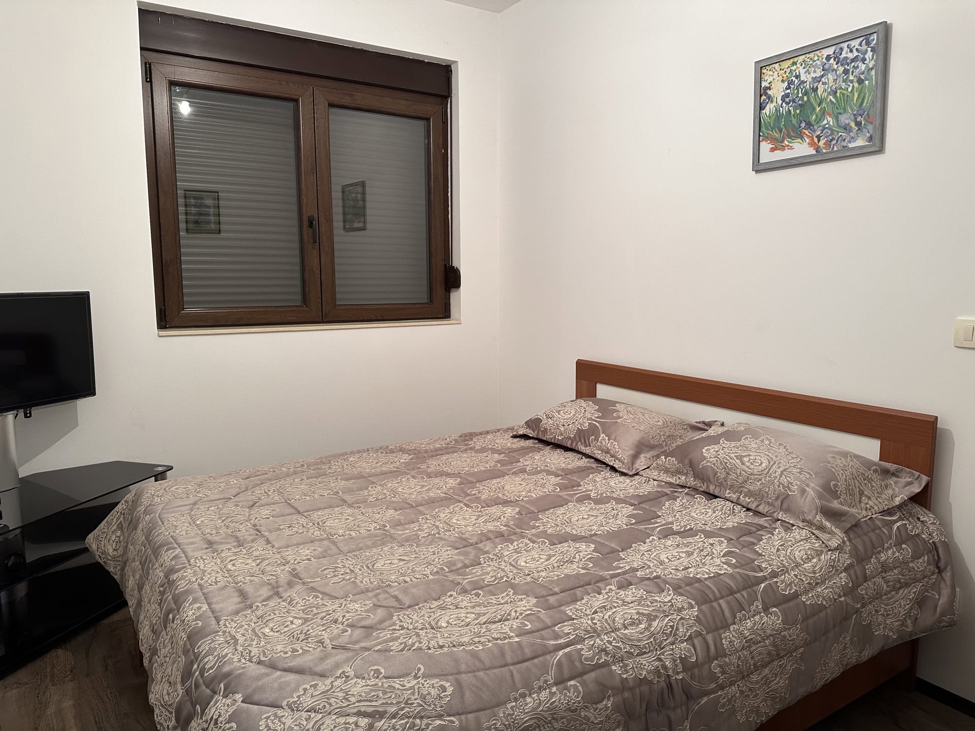 Schlafzimmer in einer Wohnung in Budva, Montenegro: Doppelbett mit gemusterter Tagesdecke, TV und Fenster mit Rollläden.