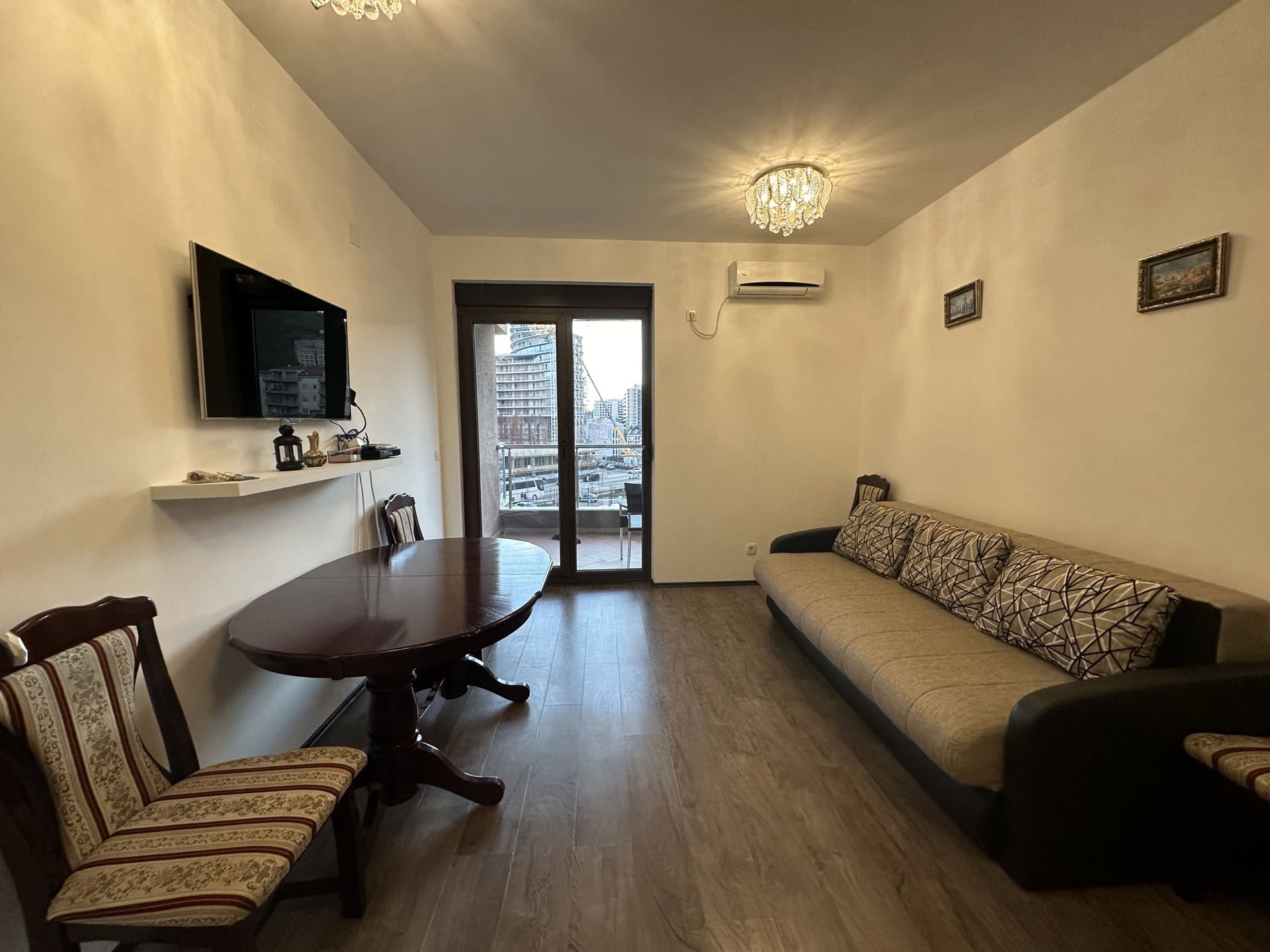 Wohnzimmer in einer Wohnung in Budva, Montenegro: Sofa, Esstisch, TV und Zugang zum Balkon mit Stadtblick.