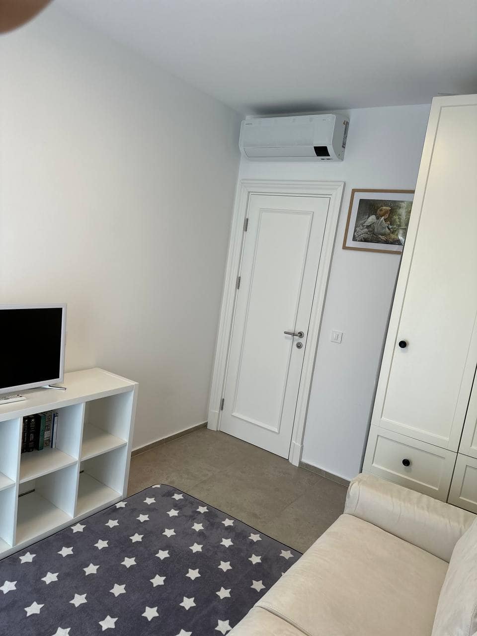 Svetla dnevna soba u stanu u Tivtu, Crna Gora: beli ormar, TV komoda, sofa i klima-uređaj u modernom enterijeru.
