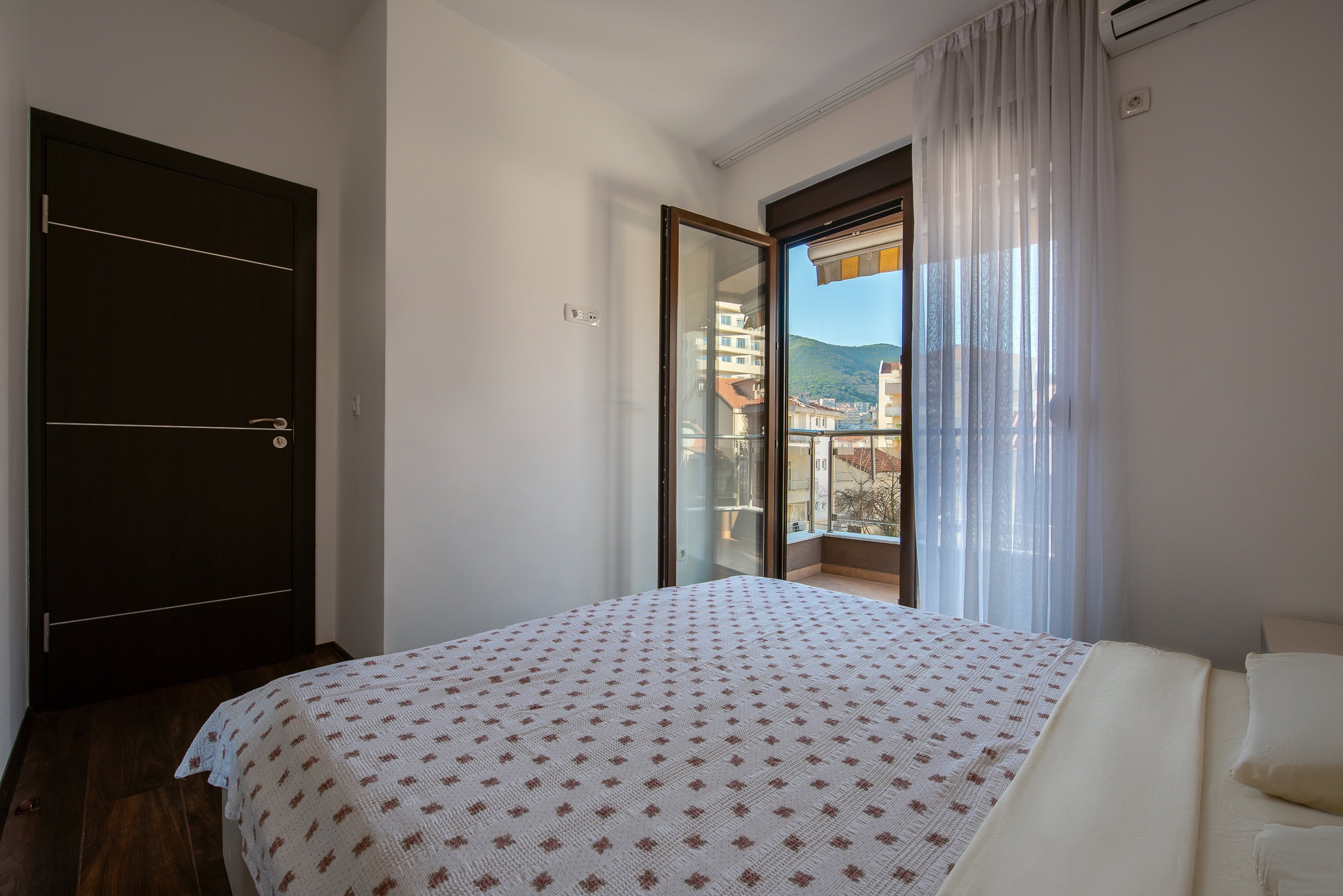 Schlafzimmer mit Doppelbett und Zugang zum Balkon mit Bergblick in einer Wohnung, Budva, Montenegro.
