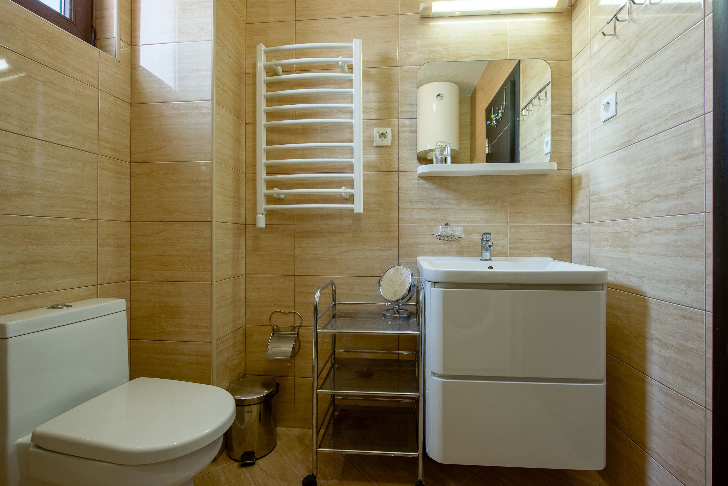 Badezimmer in einer Wohnung in Budva, Montenegro: weiße Sanitärkeramik, Handtuchheizkörper und beige Fliesen im Interieur.