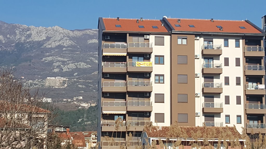 Modernes Mehrfamilienhaus mit Balkonen in Budva, Montenegro, vor malerischer Bergkulisse.