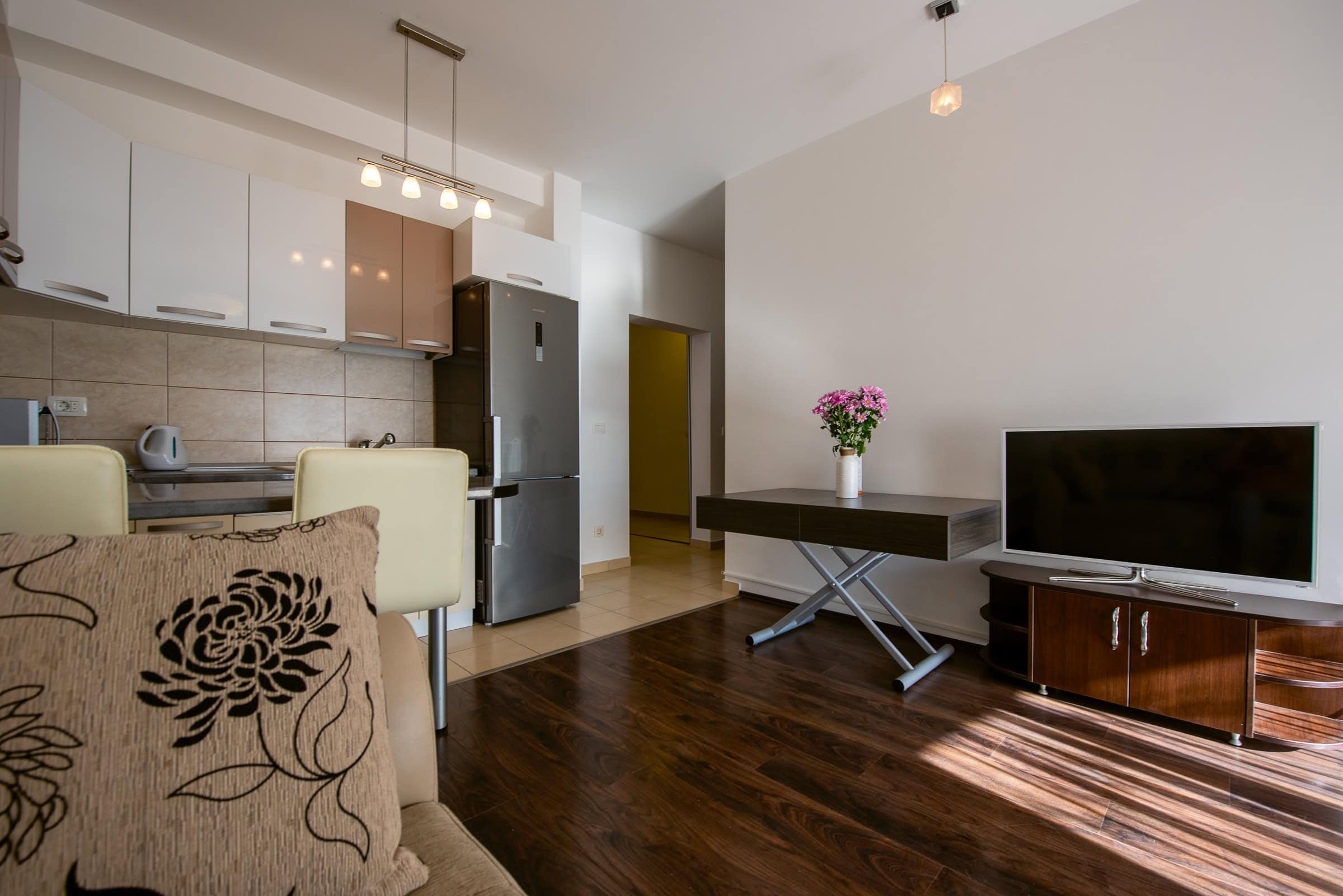 Modernes Wohnzimmer mit Küche in einer Wohnung in Budva, Montenegro: helle Möbel, TV-Bereich und Esstisch.
