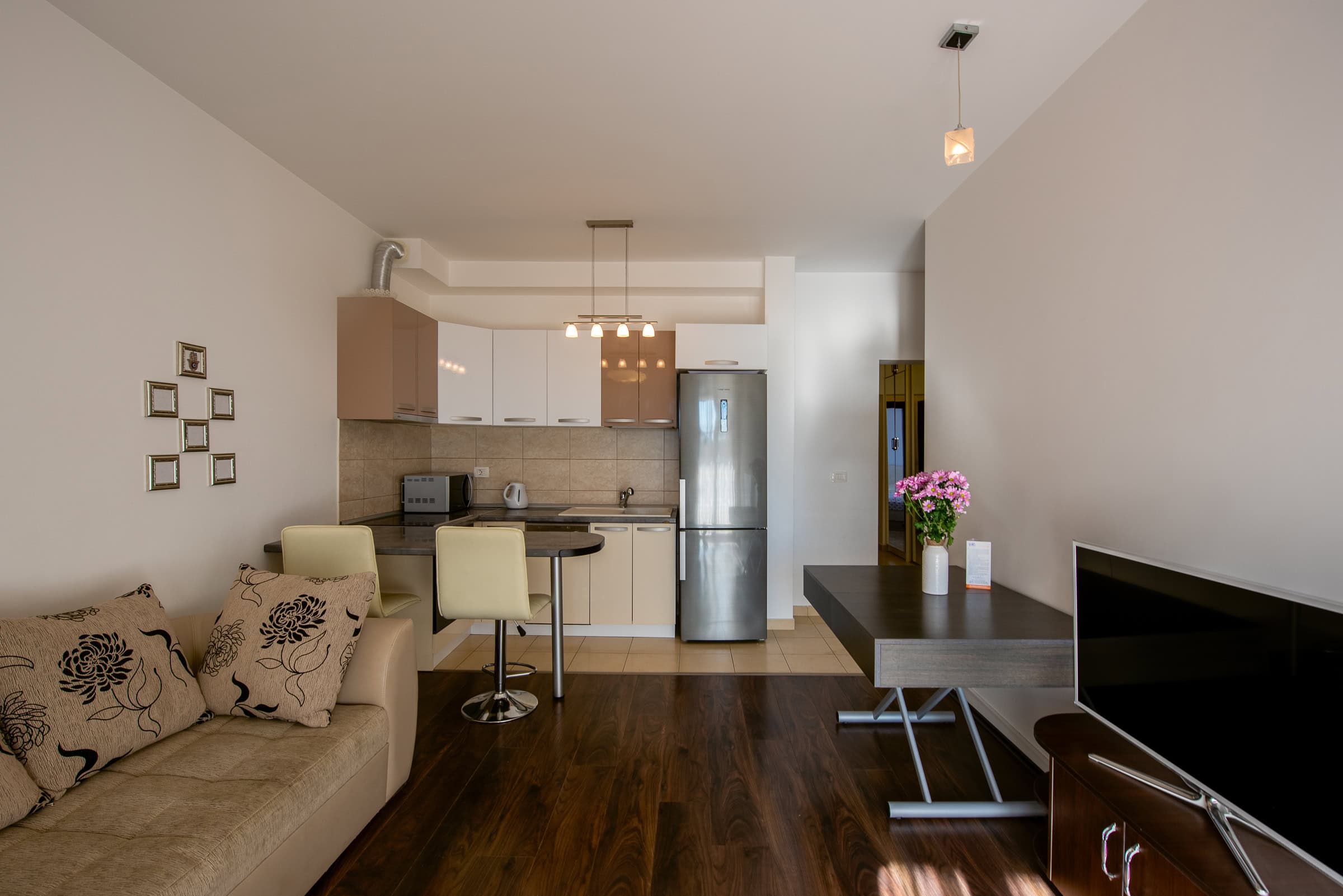 Modernes Wohnzimmer mit Küche in einer Wohnung in Budva, Montenegro: Sofa, Esstisch, Küchenzeile und TV-Bereich.