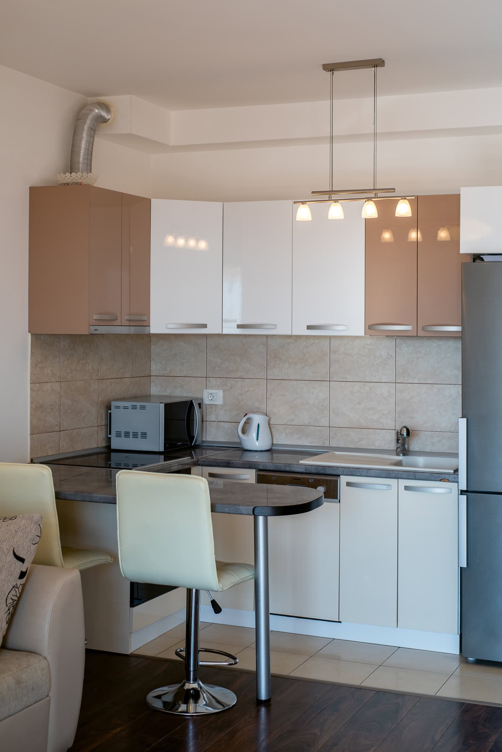 Moderne Küche in einer Wohnung in Budva, Montenegro: beige-weiße Einbauküche, Bartheke, Einbaugeräte und Spüle.