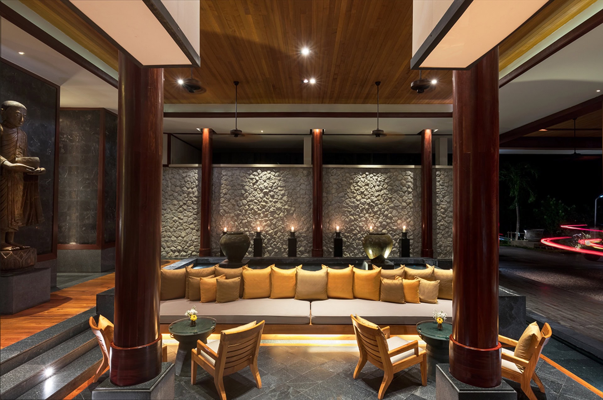 Luxuriöses Wohnzimmer mit Holzsäulen, Steinwand und weichem Sofa in einer Wohnung in Phuket, Thailand.