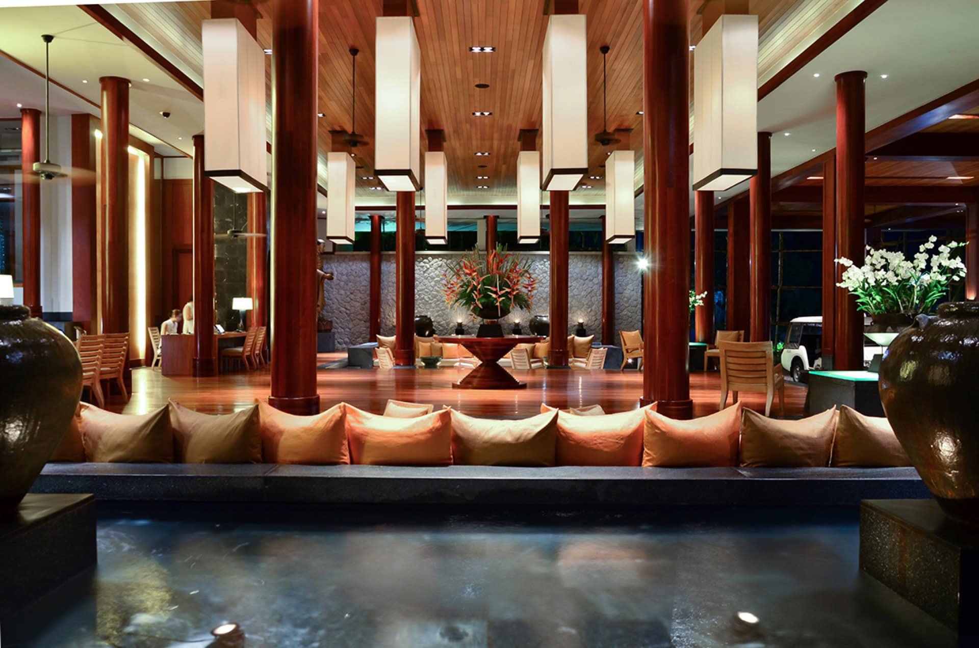 Luxuriöses Hotellobby-Interieur auf Phuket mit Holzverkleidung, Säulen, dekorativem Becken und weichen Sitzmöbeln.